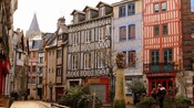 Bust of a man on a pillar in front of a row of charming timber buildings