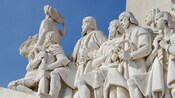 A statue of men following an explorer who is carrying a miniature ship