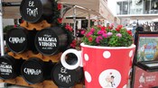 A área de estar de um restaurante perto de uma xícara gigante cheia de flores e barris com rótulos que dizem El Pimpi, Campos e Málaga Virgen