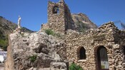 A stone building with a bell, a statue of Jesus Christ and a sign that reads Regalos La Ermita