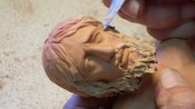 Uma mão esculpindo um rosto de estatueta barbado