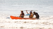 A person in the water pushing a kayak with people wearing life vests