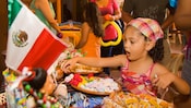 A young girl stares in awe at a table full of sweets as adults and other children mill about behind her