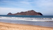 A body of water bordering a stretch of sand with an island in the distance