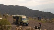Guests standing on a mountain range and taking in the views while a military style utility van stands parked nearby