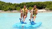 Two women peddle an aqua cycle around the lagoon with the island in the background