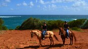 Two people on horseback, posing for a picture in front of a beach