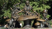 Statue of Alice sitting cross legged on a toadstool with a rabbit wearing a blazer and a man in a top hat
