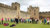 30 kids stand in a line on a castle field watching a man in costume as parents look on