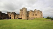 Alnwick Castle and an expansive grassy field under cloudy skies