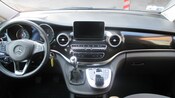 A van’s dashboard with a manual stick shift, backup monitor and keys in the ignition