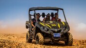 People wearing bandanas and sunglasses driving in a UTV vehicle across rocky terrain