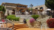 El exterior de una Hacienda con arcos, escaleras y trabajos de hierro forjado revela un patio con plantas, sillas y mesas.