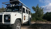 A 4 by 4 vehicle with a large roof rack, parked in the wilderness