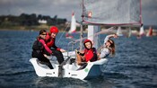 Un grupo de cuatro jóvenes que saludan sentados en un pequeño velero para cinco personas