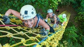 A group of young people climbs a rope ladder into the treetops