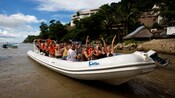 Passengers aboard a long boat pose for a picture, waving at the camera