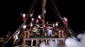 Os jogadores em um show pirata escalam e dançam no convés de um navio pirata, com fumaça subindo do chão