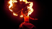 A performer in tribal dress dances with fire during an evening show