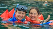 A mother and son in snorkel gear pose in shoulder deep water