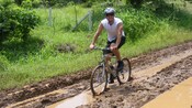 A man rides a bike along a muddy road