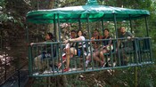 Un guía turístico y cinco visitantes sonríen mientras están sentados a bordo de una góndola al aire libre en la selva tropical