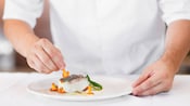 A person tops a piece of fish with mushrooms