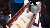 Miel de maple que se vierte desde una jarra sobre una fuente de nieve