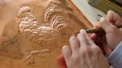 An artist uses a tool to create an embossed copper rooster design
