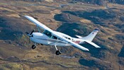 A turboprop aircraft flies over a volcanic landscape with a meandering river