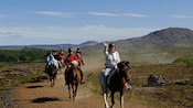 Um grupo de cavaleiros passa por uma paisagem de montanha verdejante