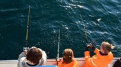 Un&nbsp;adulto y dos&nbsp;niños en una embarcación, con líneas de pesca en el agua