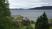 A collection of wooden huts near trees and a body of water
