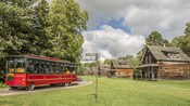 An old fashioned tour bus drives down a narrow road near a row of wooden houses in the countryside