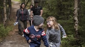2 siblings hold hands and smile as they hike up the trail with their family