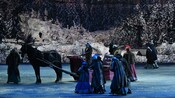 On stage, a horse and carriage and its passengers walk on a frozen lake as snow falls