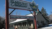 Snow surrounds a wooden clapboard building with a sign that reads Elmhurst Outdoors, Maple Sugar Farm, Skiing, Snowshoeing