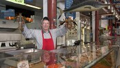 A worker at a fish market counter holds up a lobster in each hand
