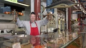 A fishmonger stands behind a counter at the Old City Market holding up a lobster in each hand