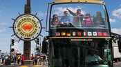 A tour guide gestures at something from the top, open air section of a double decker bus