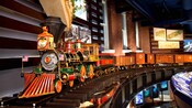 A realistic looking electric train moves over tracks in a modern museum with brownstone walls