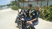 Three people in wet suits with smile at the camera while making an A OK hand gesture