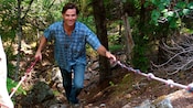 A man holds onto rope handrails as he climbs up a mountainside trail