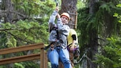 A woman in a helmet holds on to the strap of her harness as she begins her zip line adventure through the trees