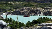 A tour group paddles a canoe with motor turned off next to a rocky riverbank