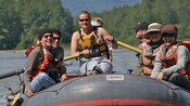 A young woman in a life vest paddles an inflatable raft carrying 7 other people