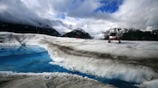 A helicopter parked on top of the snowy banks of a placid river in the mountains