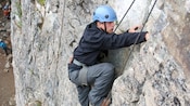 Un joven equipado con casco, arnés y cuerdas para escalar avanza por las grietas de una pared de roca