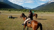 Una niña y un hombre andan a caballo en un valle boscoso cubierto de césped