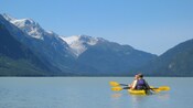Dos&nbsp;personas pasean en kayak cerca de una cadena montañosa boscosa
